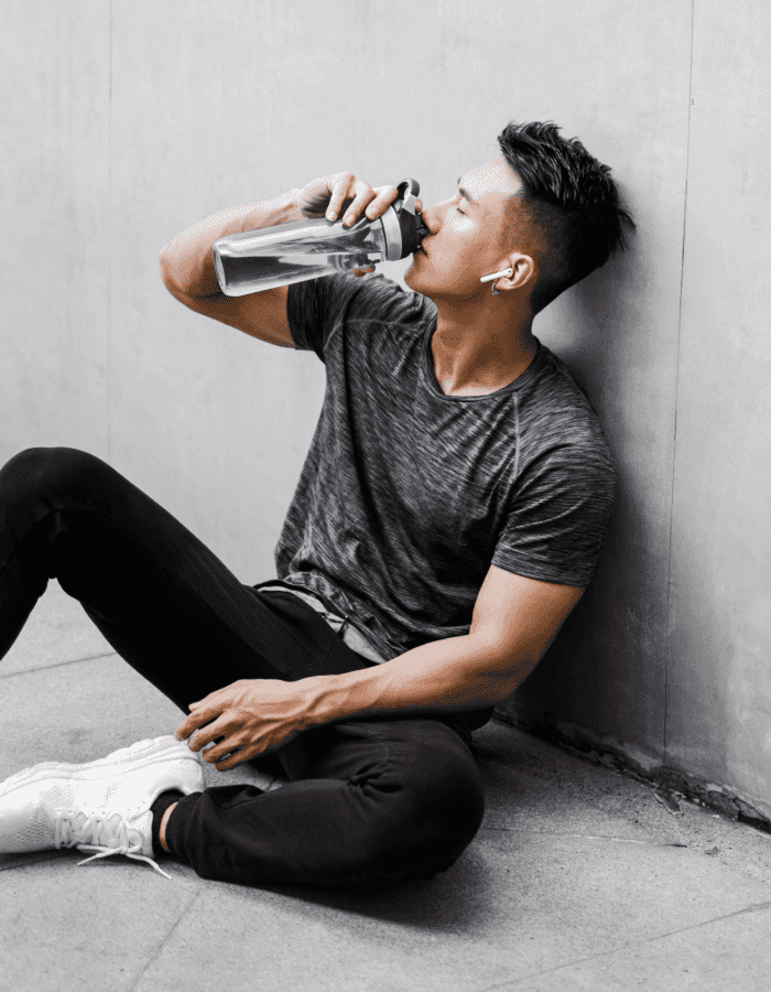Dark haired man hydrating drinking from a water bottle against wall